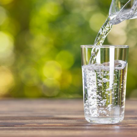 water from jug pouring into glass on wooden table outdoors