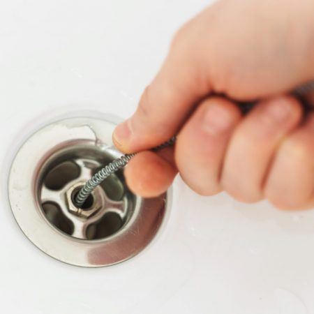 Plumber using drain snake to unclog bathtub.